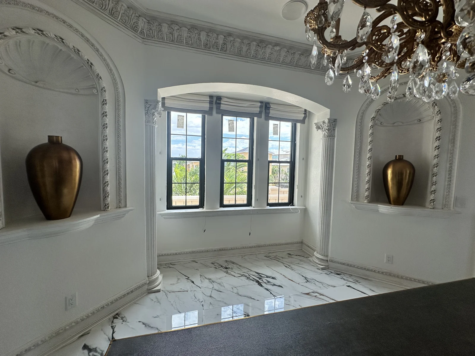 Three dark-framed rectangular windows beneath an arched opening in a bright white room with a chandelier.