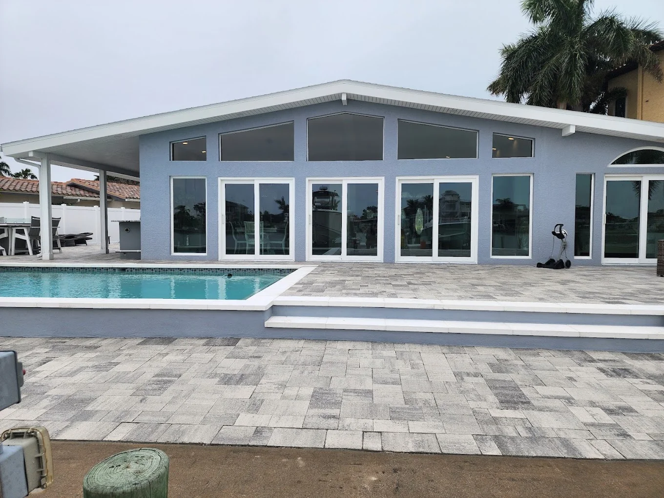 Light gray house with white-framed windows and glass doors beside a swimming pool.